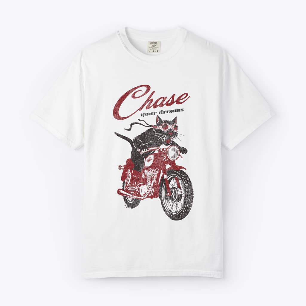 Black cat riding a red motorcycle with script text reading Chase your dreams on a white Comfort Colors t-shirt